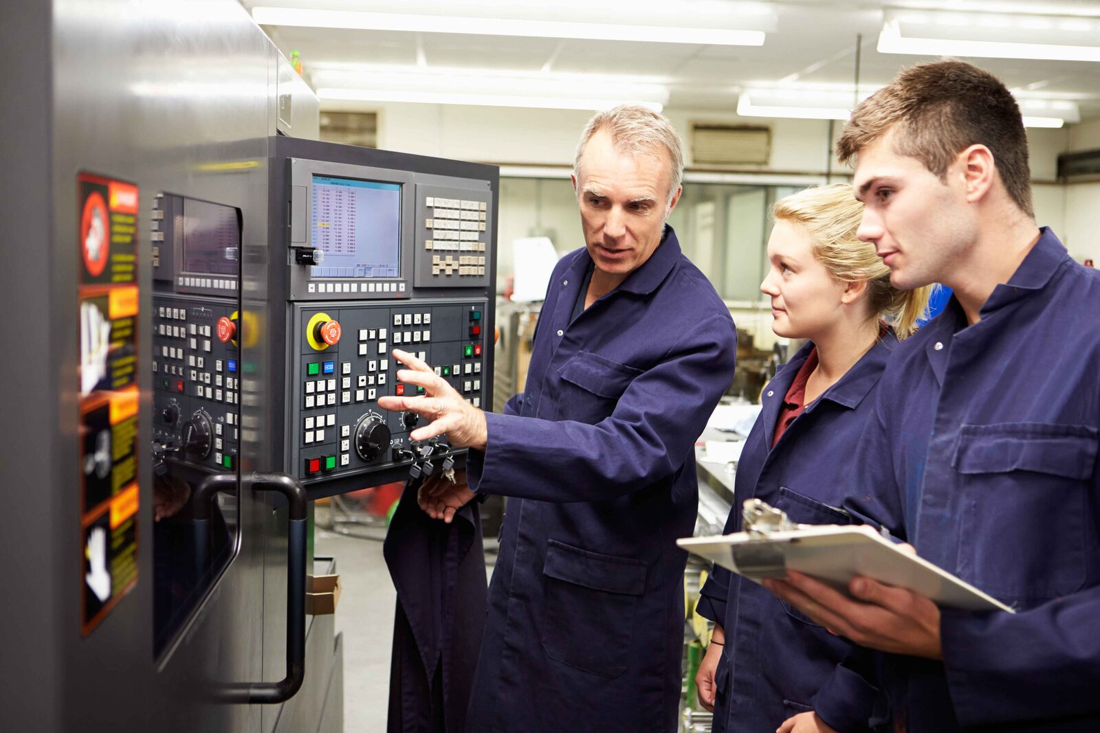 Assessor with a clipboard observing workers at industrial machinery